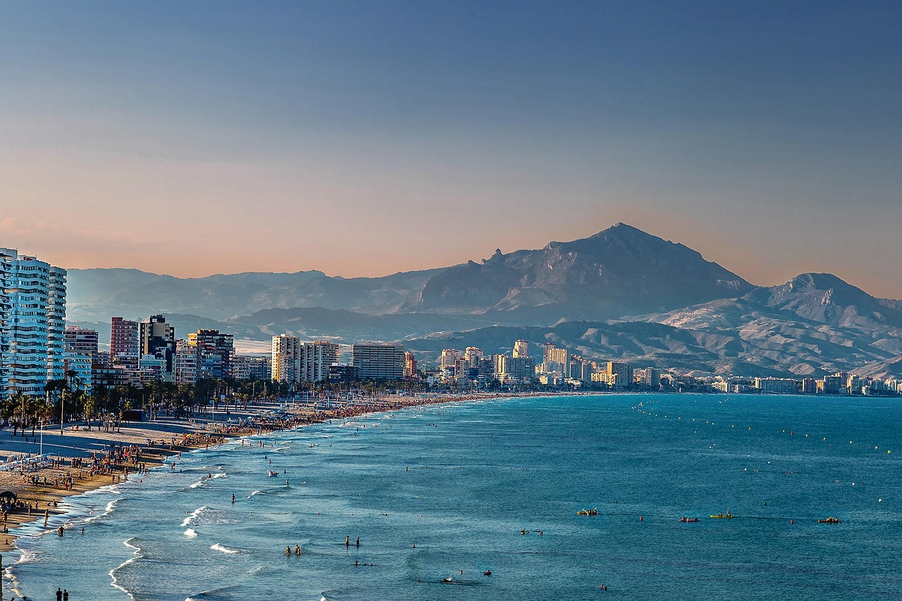 Spiaggia soleggiata della costa spagnola con onde e palme, ideale per una vacanza estiva.