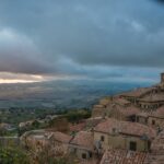 Vista panoramica del borgo toscano, con colline verdi e case in pietra, al tramonto.