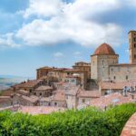 Vista panoramica di una città toscana durante un festival, con bandiere colorate e gente che partecipa.