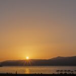 Spiaggia greca con acqua cristallina e romantico tramonto sul mare.