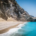 Spiaggia nascosta in Grecia con sabbia bianca e acque turchesi, immersa in un paesaggio mozzafiato.